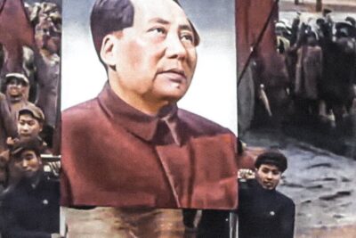 Large portrait of a political leader carried through a crowded public rally with banners and raised fists, useful for tesisin tekeminen.