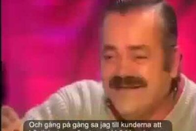 Close-up of a laughing mustached man in an interview setting with Swedish subtitles visible — tid spanien