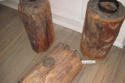 Three rustic hollowed log stools on a wooden floor, showing weathered bark and top openings til at 4.