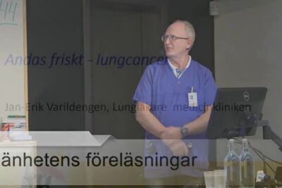 Medical professional in blue scrubs presenting a lecture slide about lung cancer and tobaksrelaterade sjukdomar