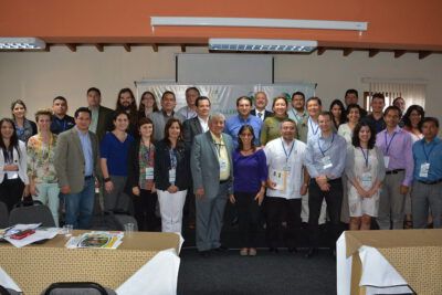 Large group of professionals posing in a conference room with badges and a presentation screen, toma decisiones 1