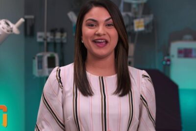 Smiling woman speaking to camera in a clinical exam room with medical equipment and teal lighting, transplantation organer 1.