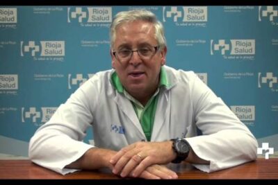 Medical professional in a white coat seated before a health service backdrop addressing trastornos ansiedad and anxiety care.