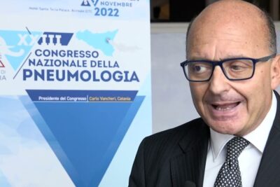 Speaker in a suit at a national pneumology congress standing beside a poster referencing trattamento dellasma