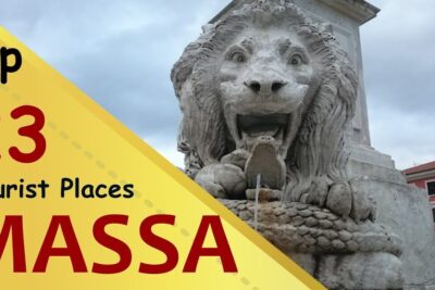 Stone lion fountain in a city square framed by a yellow promotional banner for turism massas 1.