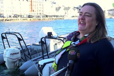 Woman smiling during a harbor interview with inflatable boats and waterfront buildings behind for turisme ogsa