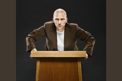 Young person leaning on a wooden podium wearing a brown blazer and white shirt, unga manniskor