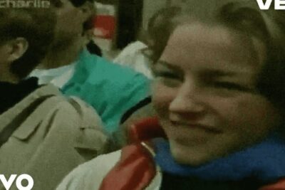 A group of unge mennesker smiling and bundled in coats and scarves in a grainy crowd photo.