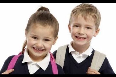Two smiling primary-aged children wearing navy v-neck sweaters, white collars and backpacks representing uniforme escolar 11.