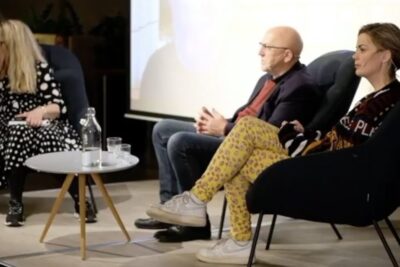 Three seated panelists and a small round table with a water bottle and glasses during a public discussion about universell grunninntekt 1