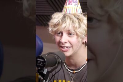 Young person with blonde curls and party hat speaking into a microphone, suitable for uomini transgender topics