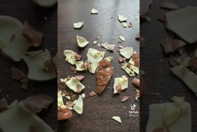 Broken milk and white chocolate shell with scattered fragments on a dark wooden surface, vaite roskaruoka.