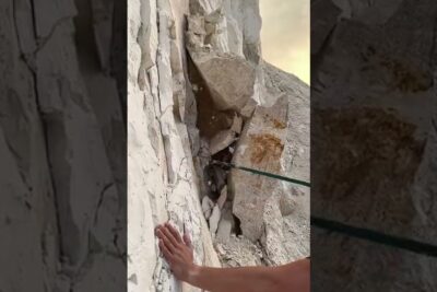 Hand of a climber pressed against a white chalky cliff with a rope for protection, valge spil visible