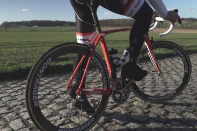 Cyclist on a red road bike riding over cobblestones illustrating the vare fordel of durable wheels and frame.