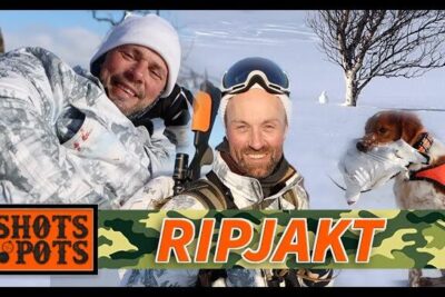 Two hunters in winter camouflage with a hunting dog holding a downed bird in a snowy varldens jakt scene