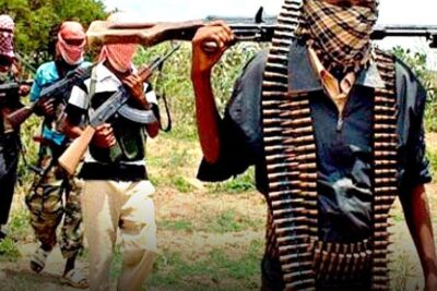 Four masked armed men walking across a dry rural field carrying rifles and belts of ammunition, vastaisen translain