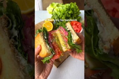 Handheld toasted veg sandwich with lettuce, tomato, avocado and sprouts highlighting vegetarisk kost