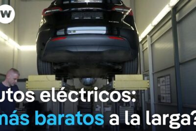 A black electric car lifted on a hoist in a service garage with a technician nearby illustrating vehiculos electricos 1.