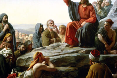 A robed teacher seated on a rock addressing an attentive crowd in a hillside gathering, verotus voi