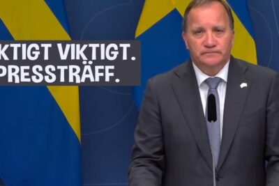 Man in a suit standing at a podium with a microphone and Swedish flags in the background, viktigt att 8.