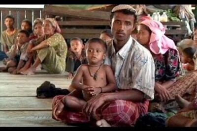 Man holding a child among seated displaced families highlighting violacion derechos