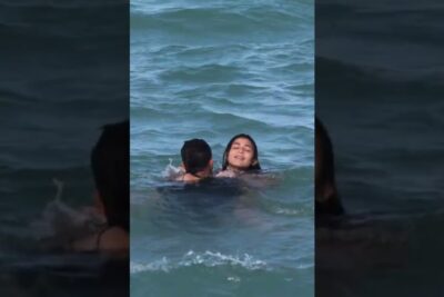 Two swimmers in the sunlit sea, one smiling and floating serenely while a companion supports them — Sunlit Sea Swim with Smiling Swimmer — virtuelle verdenen 1 Beach Portrait