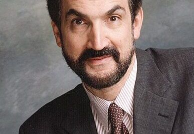 Bearded man in a dark suit and patterned tie looking at the camera, voi auttaa 1