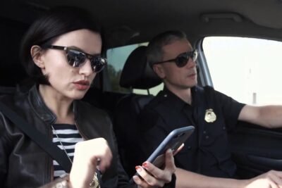 Two uniformed officers in a patrol car discussing voluntary departure while one checks a smartphone