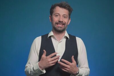 Smiling man in white shirt and dark vest gesturing while explaining vor nachteile 3.