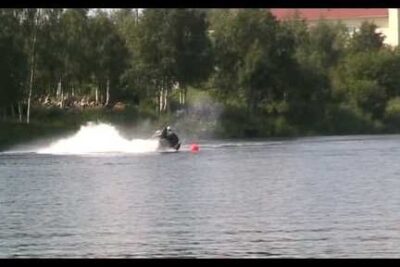 Person riding a jet ski across a calm lake with spray and a red buoy in view, vuonna 2006.