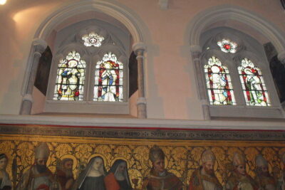 Arched stained glass windows above a painted religious frieze in a church interior, windows 11 2.
