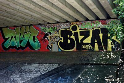 Colorful graffiti mural under a concrete bridge with bold yellow and green tags and layered street art emphasized for yhteiskunta 6.
