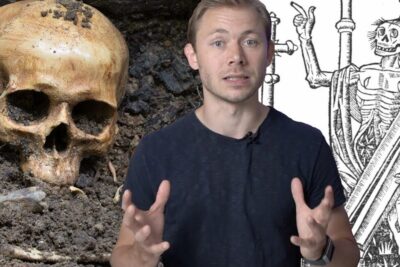 Presenter gesturing before a partially buried human skull and a medieval skeletal woodcut about zombier virkelige.