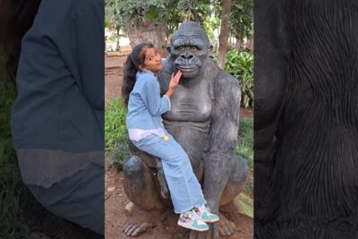 Girl sitting on a gorilla statue in a leafy park, zoologiske haver 3